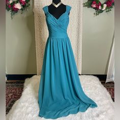 a blue dress is on display in front of a white wall and flowers behind it