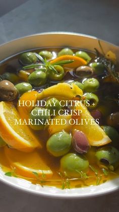 a white bowl filled with olives, oranges and other fruits next to the words holiday citrus chili crisp marinated olives