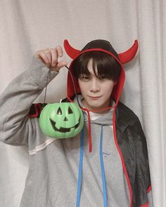 a young man wearing a devil costume and holding a green pumpkin