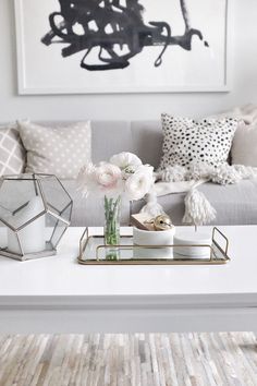 a living room filled with furniture and flowers on top of a coffee table in front of a painting