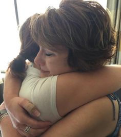 two women hugging each other in front of a window