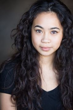 a young woman with long curly hair posing for a photo and looking at the camera