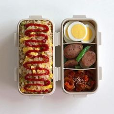 an open lunch box with eggs, sausages and rice in it on a white surface