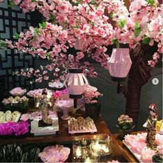 a table topped with lots of pink flowers next to a lamp and vases filled with food