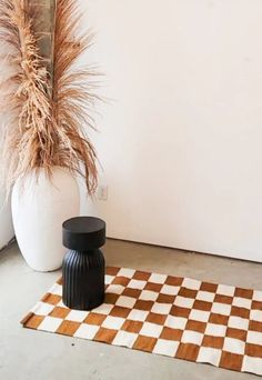 a black and white vase sitting next to a brown and white checkerboard rug