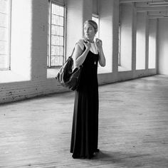 a woman standing in an empty room holding a handbag