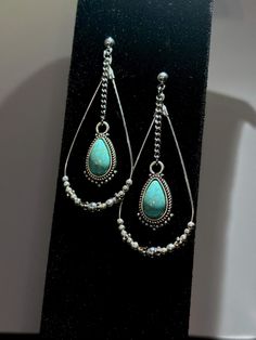 Show off your charm with these southwestern statement hoop earrings, featuring a teardrop-shaped resin turquoise pendant and an array of round silver and daisy spacer beads! Delicately handcrafted and designed, these unique and captivating earrings make a wonderful accent to any outfit! DETAILS: > Dimensions: ~2.5in L x ~1.05in W  > Earring Weight (both): ~.25oz > Nickel-free & hypoallergenic!  > Copper hoop, metal chain, 100% iron ball post earwire with clutch, brass findings, resin pendant > Jewelry findings are gently cleaned, applied with an anti-tarnish shield, and delicately polished. HIGHLIGHTS: > PENDANT: This beautiful teardrop-shaped pendant is made out of shiny resin and durable metal alloy, creating a stunning turquoise look!  > HOOP: The bead pattern on these teardrop hoops co Southern Jewelry, Teardrop Hoop Earrings, Turquoise Hoop Earrings, Turquoise Hoops, Statement Hoop Earrings, Western Earrings, Earrings Everyday, Jewelry Turquoise, Earrings Unique