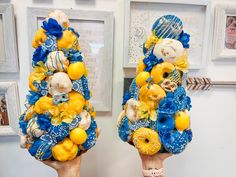 two hands holding up fake lemons and blue flowers in front of pictures on the wall