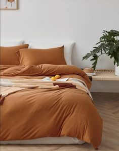 a bed with an orange comforter on top of it next to a potted plant