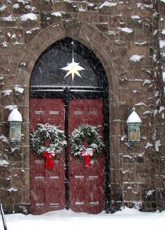 two red doors with wreaths on them in front of a brick building covered in snow