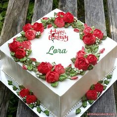 a white cake with red roses on it sitting on a wooden bench in the grass