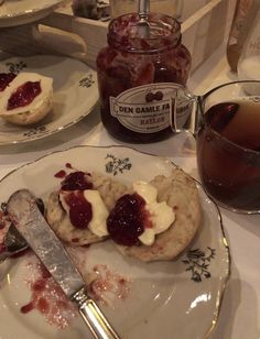 a plate with jam and biscuits on it next to a glass of tea in front of a jar