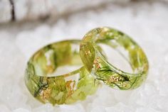 two green wedding rings sitting on top of a white table covered in ice and snow