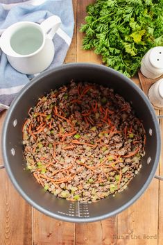 a pot filled with carrots and meat on top of a wooden table next to some parsley