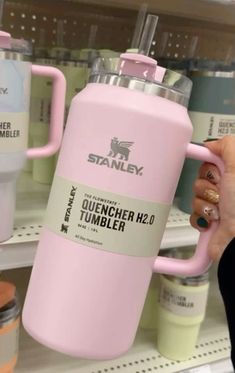 a person holding a pink coffee cup in front of some shelves with tumblers on it