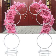 two circular metal sculptures with pink flowers on them in front of a red door and doorway