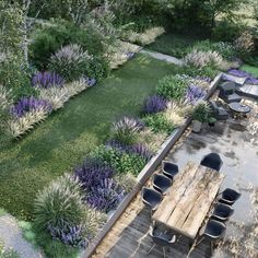 an aerial view of a wooden table and chairs in a garden with purple flowers on the ground