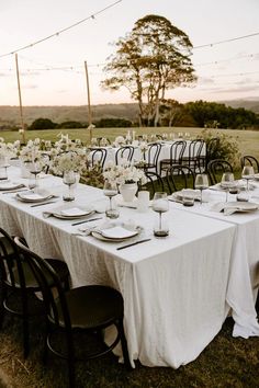 a long table set up with white flowers and place settings for an outdoor dinner party