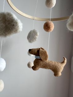 a stuffed dog is hanging from a mobile with balls on it's string and some wool balls in the background