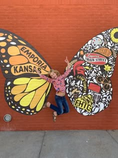 a woman standing next to a butterfly painted on the side of a building with her arms in the air