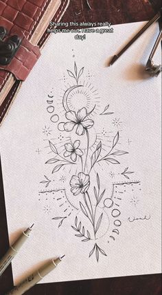 an old book with flowers on it next to some pens and pencils sitting on a table