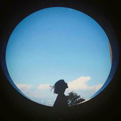 a person standing in front of a circular object with the sky and clouds behind them