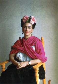 an old photo of a woman sitting in a chair wearing a pink shawl and flowers on her head