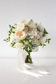 a bouquet of white flowers and greenery in a glass vase on a white surface