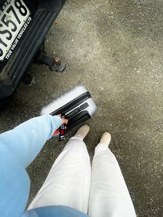 the legs of two people standing next to a parked car with luggage on it's back