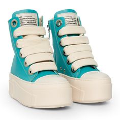 The sneakers are high-top platform-style shoes with a dominant color scheme of tiffany and cream. They feature a thick, cream-colored rubber sole with layered detailing that gives the shoe a bold and chunky silhouette. The upper part of the sneakers is primarily tiffany, constructed with leather material. The design includes metal eyelets for the laces, which are cream-colored and chunky, complementing the sole. Calipso Shoes, Leather Material, Color Scheme, Cream Color, High Top, Shoe Laces, High Tops, Rubber Sole, Color Schemes