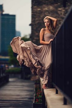 a woman leaning on a rail with her dress blowing in the wind and buildings behind her