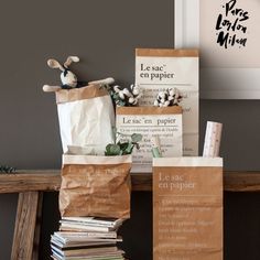 some brown paper bags sitting on top of a wooden table next to a pile of books