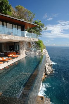 an outdoor swimming pool next to the ocean with lounge chairs on it and water running down the side