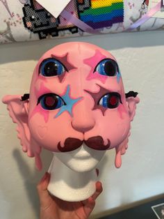 a person holding up a pink mask with blue stars on it's face and nose