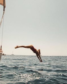 a man dives into the water from a sailboat as another boat floats in the background