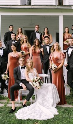 a group of people standing and sitting in front of a white house wearing formal wear