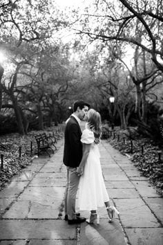 a man and woman kissing in the middle of a walkway with trees lining both sides