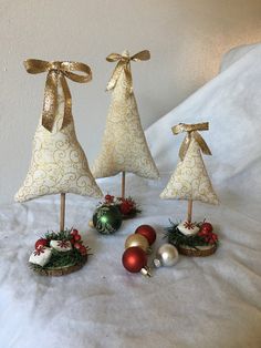 three small christmas trees with gold bows and ornaments on a white sheeted bed spread