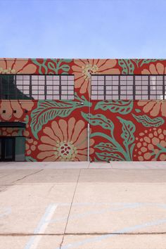 an orange and green building with flowers painted on it's side in front of a parking lot