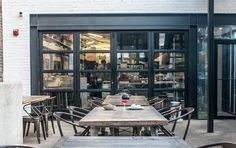 an outdoor dining area with wooden tables and chairs, in front of a storefront