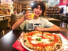 a young boy sitting at a table with a pizza and drink in front of him