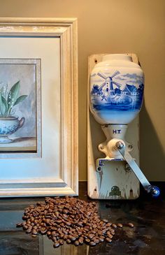 a coffee grinder sitting on top of a table next to a framed painting and beans