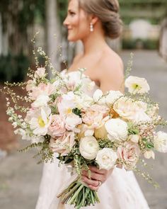 a bride holding a bouquet of flowers in her hands and looking off into the distance