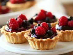 small tarts topped with berries and blueberries on a white plate