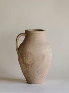 a white vase sitting on top of a table next to a gray wall and floor