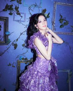 a woman in a purple dress standing next to a blue wall