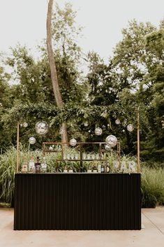 an outdoor bar with lots of bottles and glasses on the top, surrounded by greenery