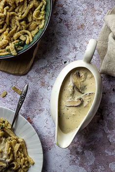 two plates filled with pasta and mushrooms next to a bowl of mushroom sauce on a table