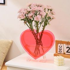 a heart shaped vase with flowers in it on a table next to a small clock