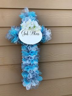 a blue and white flower cross hanging on the side of a house with god's blessing written on it